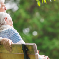 Mooie, passende afbeelding! Hier is de bijbehorende alt-tekst, een paar varianten: ALT-TEKST (SEO + toegankelijkheid) Ouder echtpaar zit samen op een bankje in de natuur, van achteren gezien — symbolisch voor samenzijn en rust