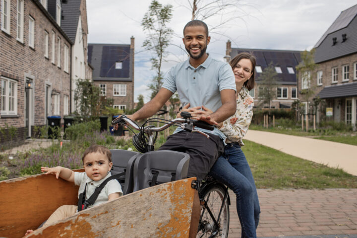 Gezin in een bakfiets in een groene, duurzame woonwijk.